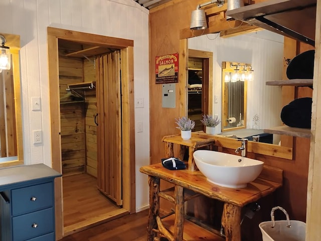 bathroom with wood walls, a sink, and wood finished floors