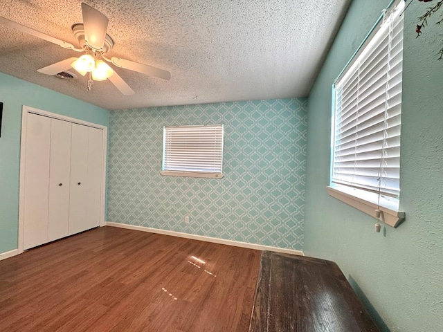 2003 N Enfield Rd, Alpine, TX 79830 - unfurnished bedroom with wood finished floors, a textured ceiling, ceiling fan, baseboards, and wallpapered walls