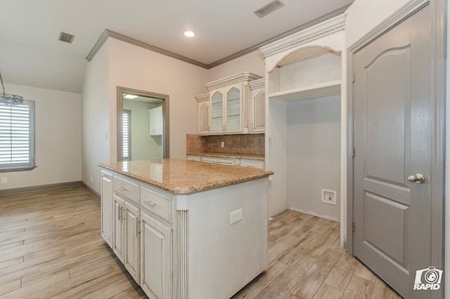 kitchen featuring decorative backsplash, a kitchen island, light wood-style flooring, glass insert cabinets, and light stone counters