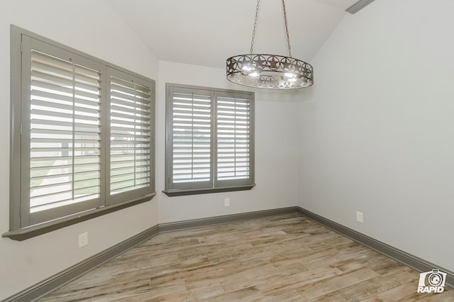 unfurnished dining area with vaulted ceiling, a chandelier, wood finished floors, and baseboards