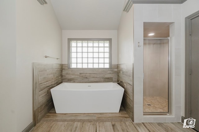 full bathroom with a stall shower, lofted ceiling, a freestanding tub, wood finished floors, and tile walls