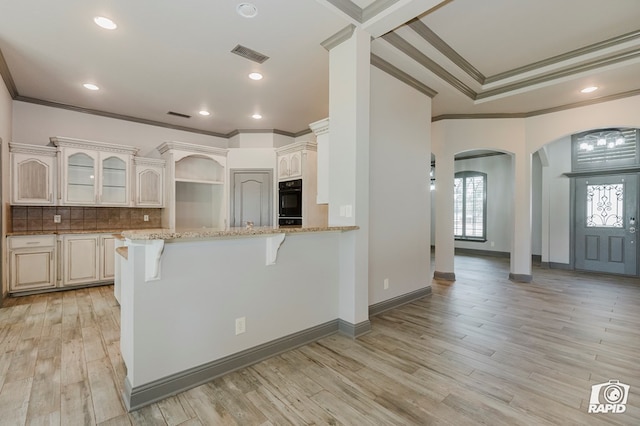 kitchen featuring arched walkways, ornamental molding, light stone counters, a peninsula, and a kitchen bar