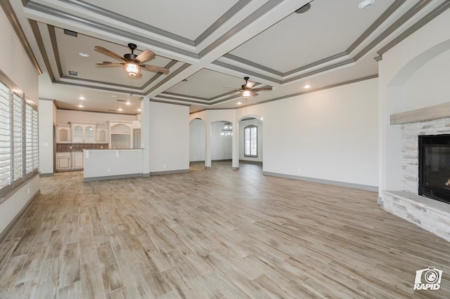 unfurnished living room featuring a ceiling fan, arched walkways, a fireplace, ornamental molding, and light wood-style flooring