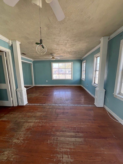 empty room with a textured ceiling, ceiling fan, ornamental molding, and dark wood-type flooring