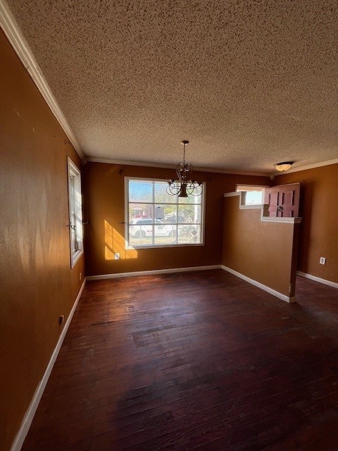 unfurnished dining area featuring dark hardwood / wood-style floors, ornamental molding, a textured ceiling, and an inviting chandelier