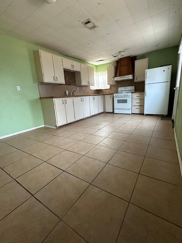 kitchen with light tile patterned floors, white appliances, custom exhaust hood, and white cabinets