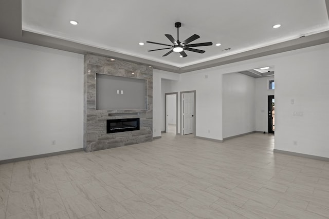 unfurnished living room featuring a tray ceiling, a large fireplace, recessed lighting, ceiling fan, and baseboards
