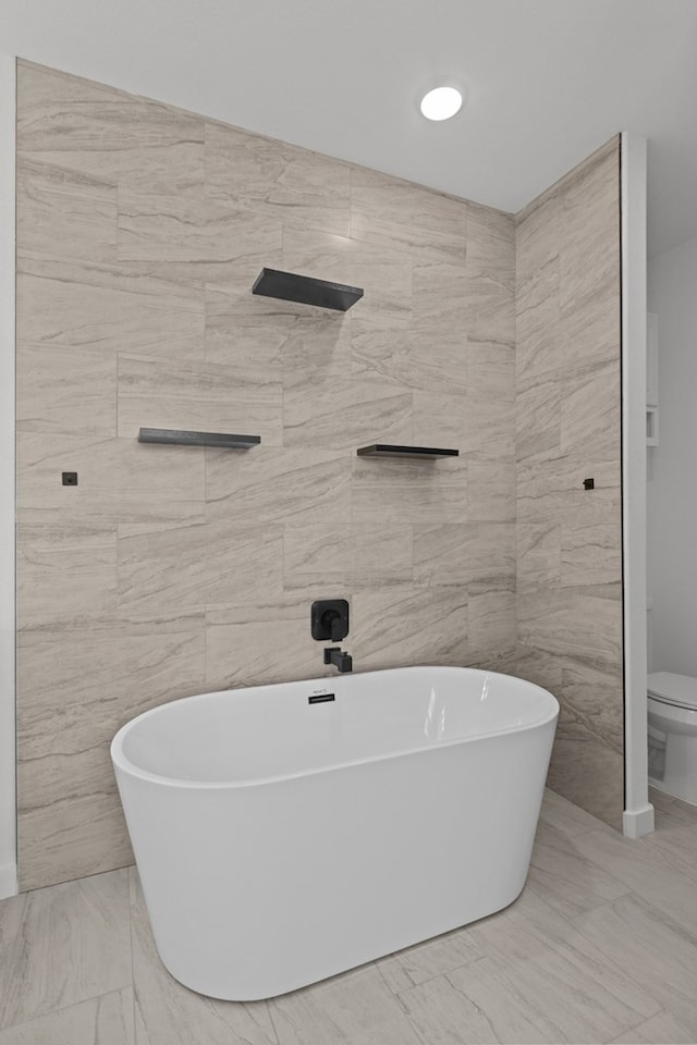 full bathroom featuring marble finish flooring, a freestanding tub, toilet, and tile walls