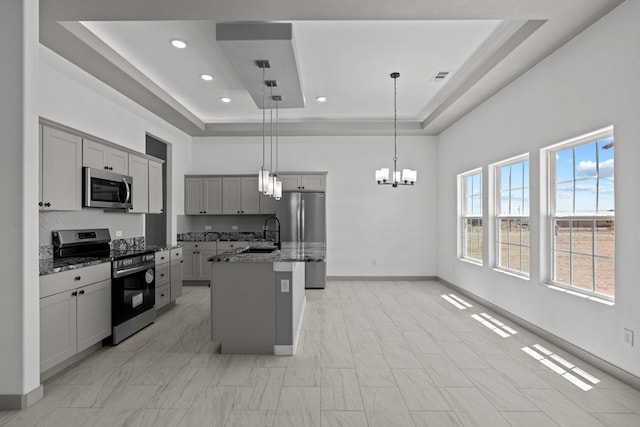 kitchen with stainless steel appliances, a raised ceiling, stone countertops, a chandelier, and a sink