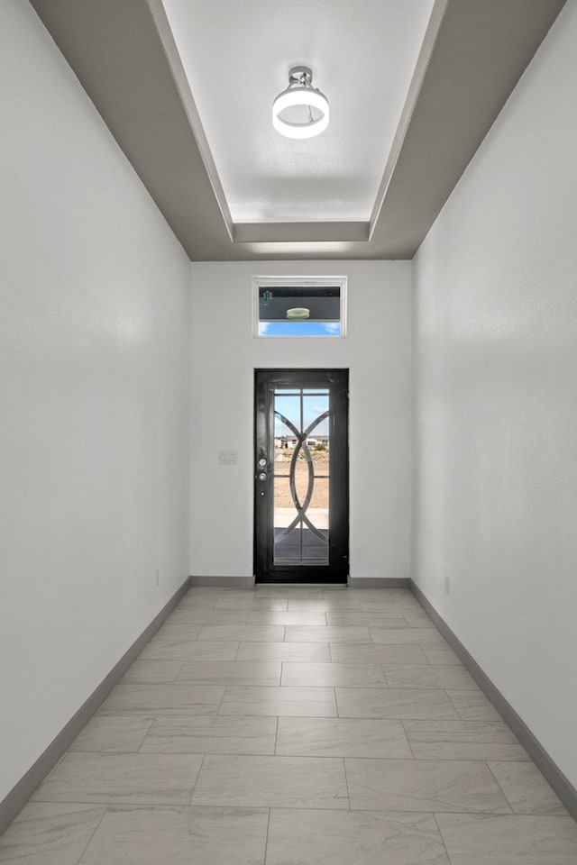 foyer entrance featuring a raised ceiling and baseboards