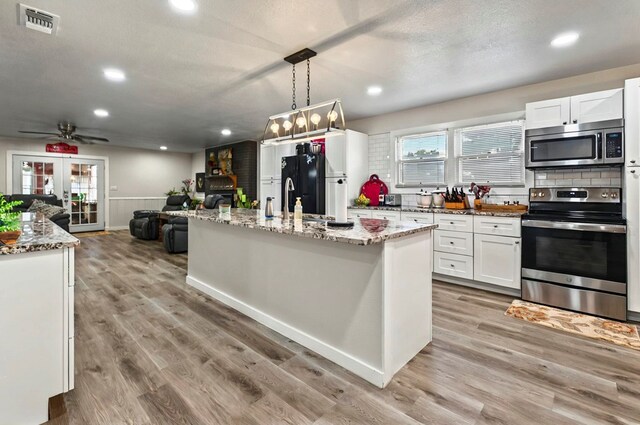 811 NW 7th St, Andrews, TX 79714 - kitchen with appliances with stainless steel finishes, white cabinetry, open floor plan, light stone countertops, and a kitchen island with sink
