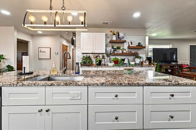 811 NW 7th St, Andrews, TX 79714 - kitchen featuring a sink, open shelves, white cabinets, stone counters, and tasteful backsplash