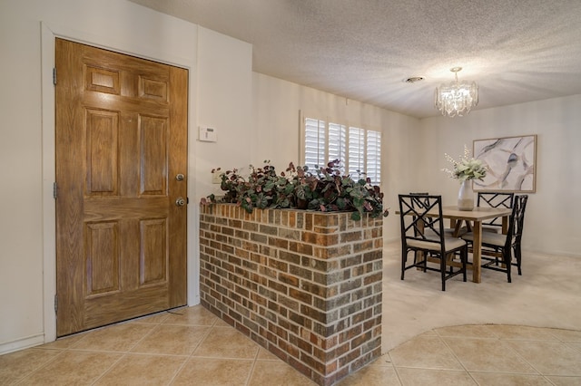 foyer entrance with light colored carpet, a textured ceiling, a notable chandelier, and light tile patterned floors