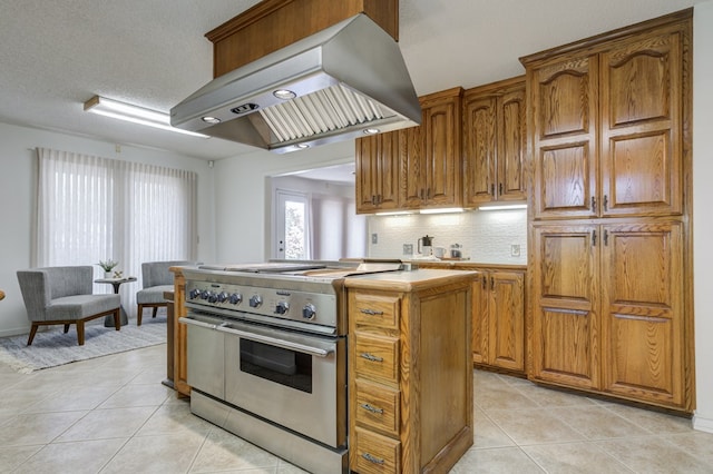 kitchen with exhaust hood, light tile patterned flooring, high end stainless steel range oven, backsplash, and a center island