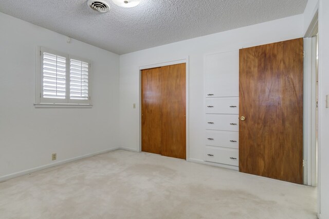 unfurnished bedroom featuring a textured ceiling, carpet flooring, baseboards, and visible vents