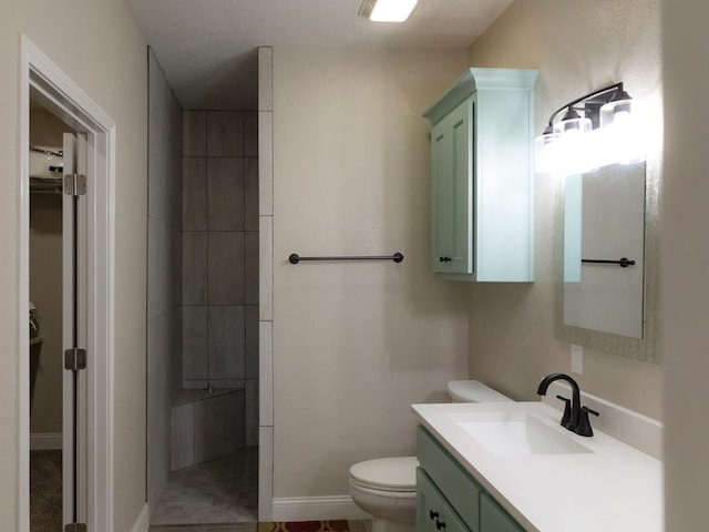 bathroom featuring toilet, vanity, and tiled shower