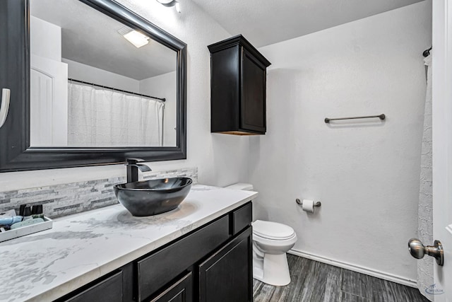 full bath featuring wood finished floors, toilet, vanity, baseboards, and tasteful backsplash