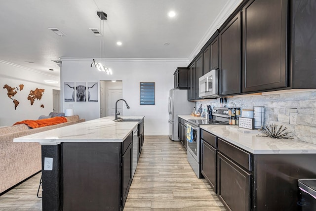 kitchen featuring stainless steel appliances, light wood finished floors, ornamental molding, open floor plan, and an island with sink