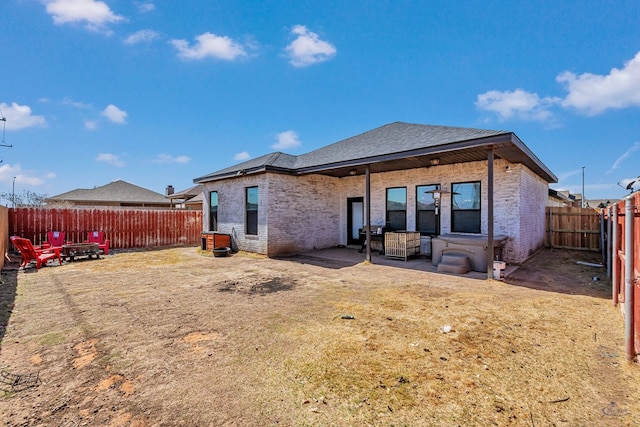 rear view of house with brick siding, a fenced backyard, a patio area, and an outdoor fire pit