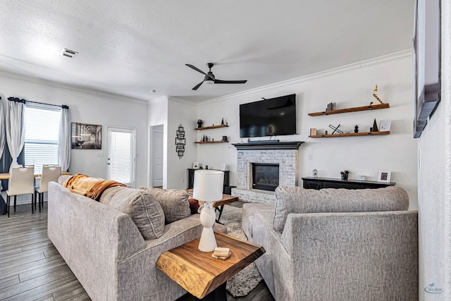 living room with ceiling fan, ornamental molding, wood finished floors, a brick fireplace, and a textured ceiling