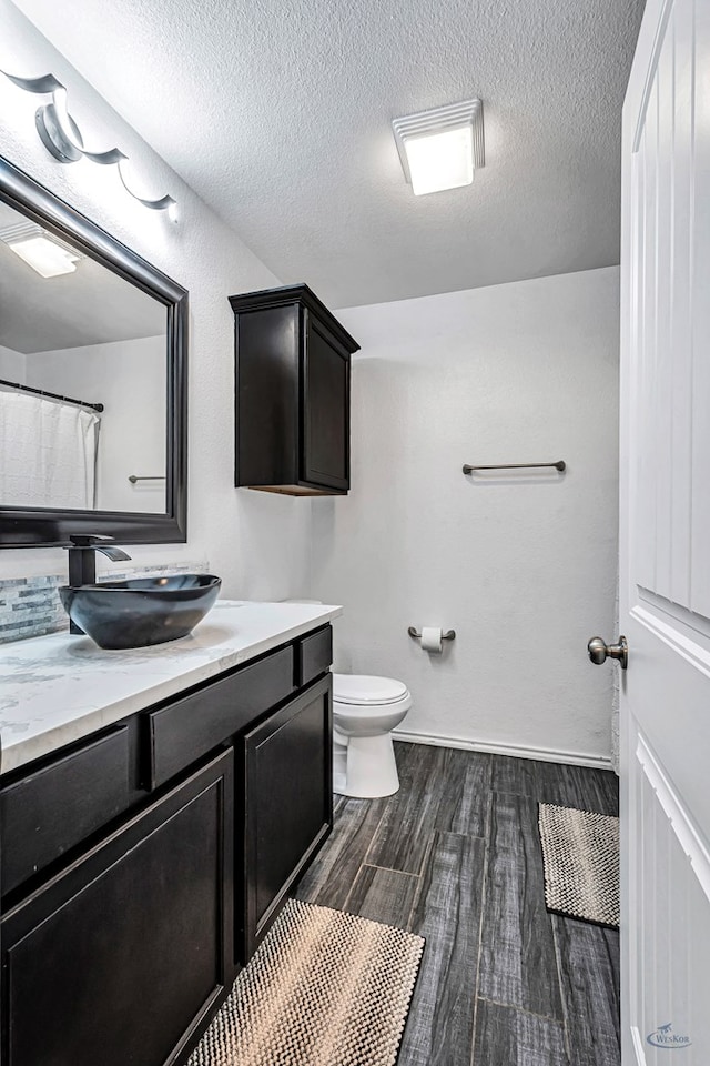 bathroom with wood finished floors, toilet, vanity, and a textured ceiling