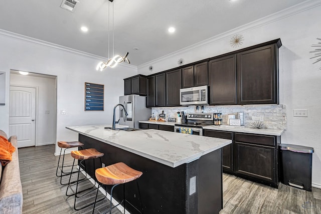 kitchen featuring appliances with stainless steel finishes, a sink, crown molding, a kitchen island with sink, and light wood-style floors