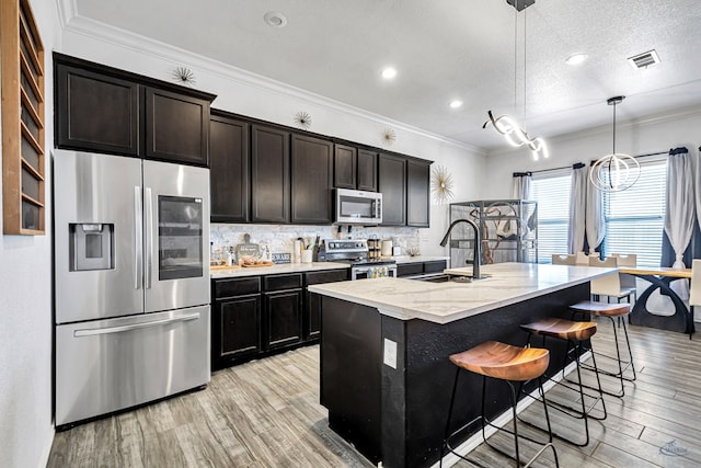 kitchen with stainless steel appliances, a sink, light wood-style floors, decorative backsplash, and light stone countertops