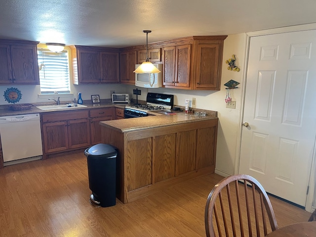 kitchen with kitchen peninsula, white appliances, sink, light hardwood / wood-style floors, and hanging light fixtures