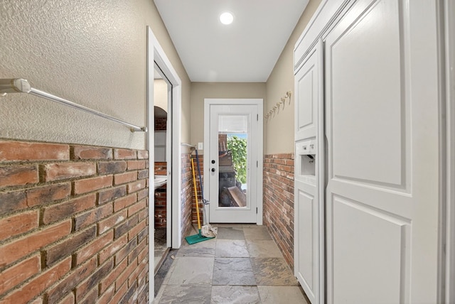2720 Fair Oaks Cir, Odessa, TX 79762 - doorway to outside with stone tile floors, brick wall, and a wainscoted wall