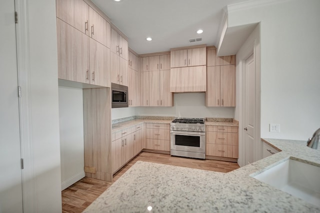 kitchen with light brown cabinetry, a sink, light stone counters, light wood-style floors, and stainless steel appliances