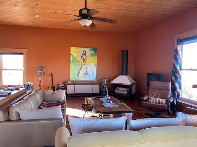 living room featuring ceiling fan, a wood stove, and wood ceiling