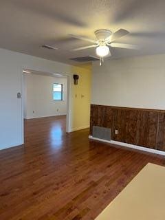 spare room featuring dark hardwood / wood-style flooring, ceiling fan, and wood walls