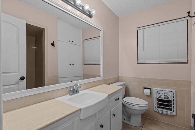 bathroom featuring tile walls, toilet, vanity, a textured ceiling, and heating unit