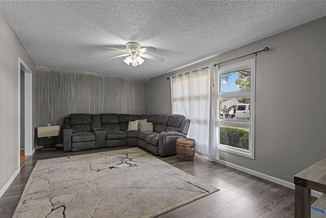 living area featuring a textured ceiling, wood finished floors, baseboards, and ceiling fan