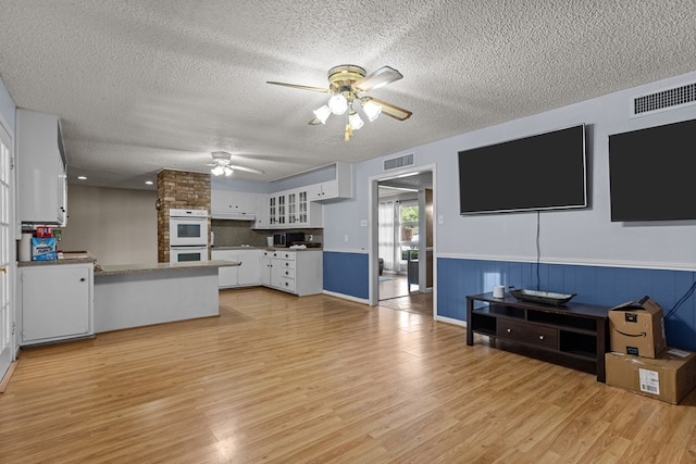 living room with light wood-style floors, visible vents, a ceiling fan, and a textured ceiling