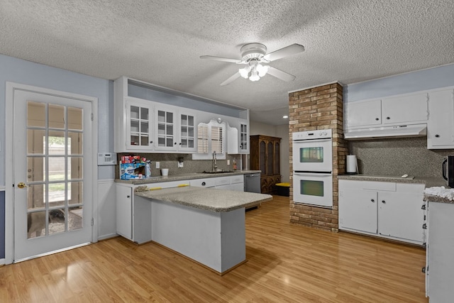 kitchen featuring a sink, a peninsula, under cabinet range hood, white double oven, and white cabinetry