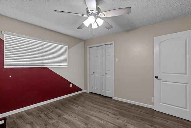 unfurnished bedroom featuring a closet, a textured ceiling, wood finished floors, and baseboards