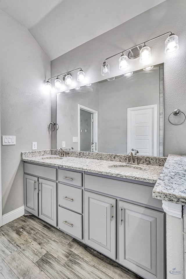 bathroom with a sink, double vanity, vaulted ceiling, and wood finished floors