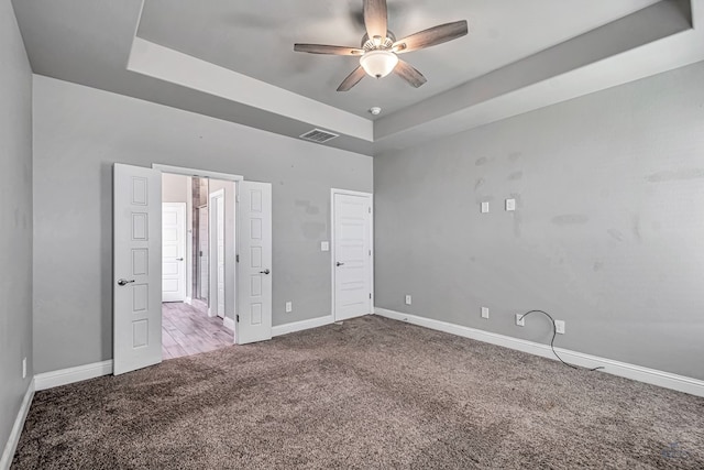 unfurnished bedroom with a tray ceiling, carpet flooring, baseboards, and visible vents