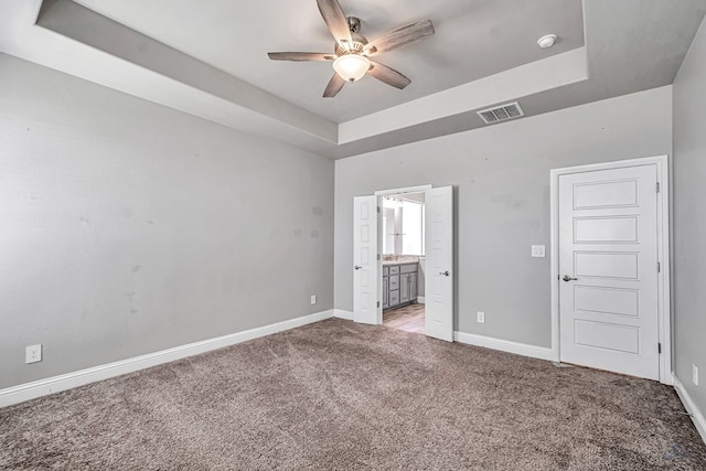 unfurnished bedroom featuring a tray ceiling, baseboards, ensuite bathroom, visible vents, and light colored carpet