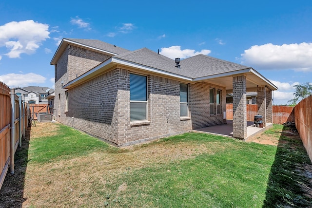 back of house featuring a lawn, a shingled roof, a fenced backyard, a patio area, and brick siding