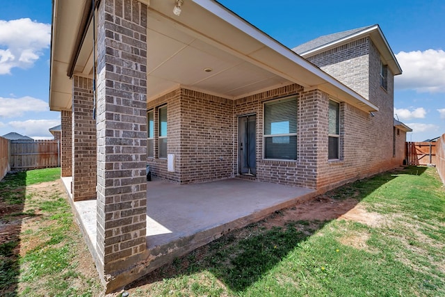 rear view of property featuring brick siding, a fenced backyard, a lawn, and a patio area