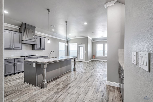 kitchen with a sink, crown molding, a textured wall, gray cabinetry, and custom range hood