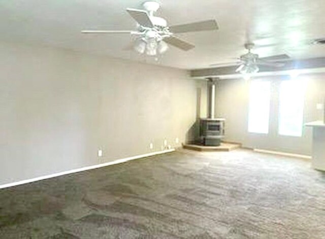 906 S Franklin Ave, Monahans, TX 79756 - unfurnished living room with a wood stove, baseboards, carpet flooring, and ceiling fan