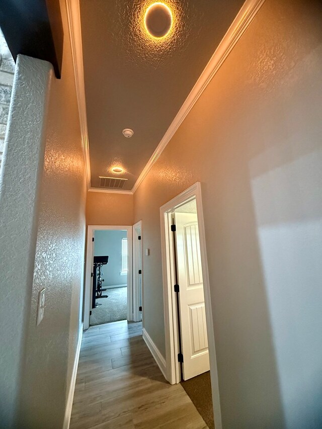 hallway featuring wood finished floors, visible vents, crown molding, a textured wall, and baseboards
