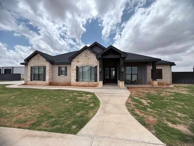 view of front of property featuring roof with shingles, french doors, stone siding, a front yard, and board and batten siding
