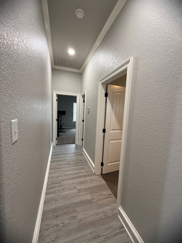 corridor with wood finished floors, crown molding, visible vents, baseboards, and a textured wall