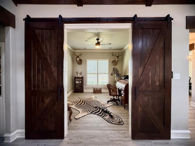 office space featuring wood finished floors, a barn door, ceiling fan, crown molding, and baseboards