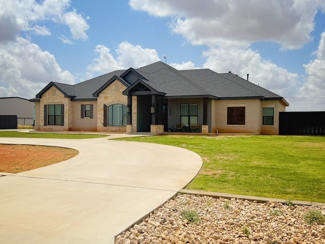 view of front of home with a front lawn, roof with shingles, curved driveway, and stone siding