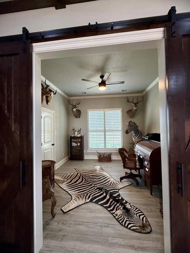 office area with a ceiling fan, ornamental molding, a barn door, and wood finished floors